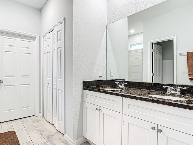 full bath featuring double vanity, a textured wall, a closet, and a sink