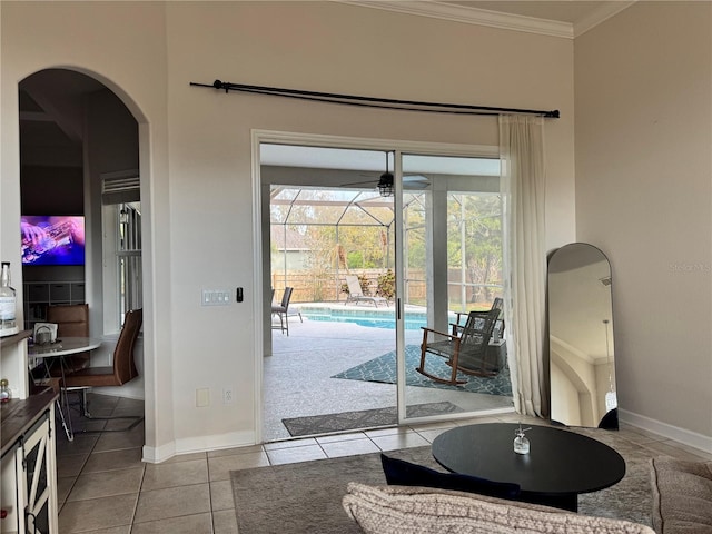 doorway to outside featuring a ceiling fan, tile patterned floors, arched walkways, baseboards, and ornamental molding
