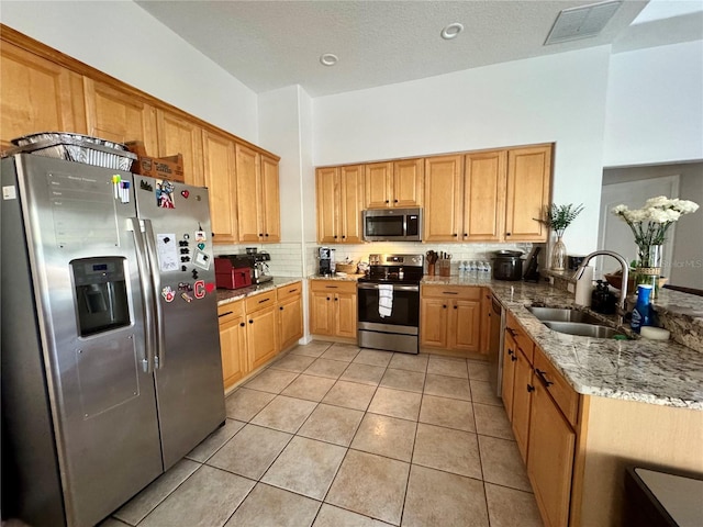 kitchen with a sink, decorative backsplash, light tile patterned floors, appliances with stainless steel finishes, and light stone countertops