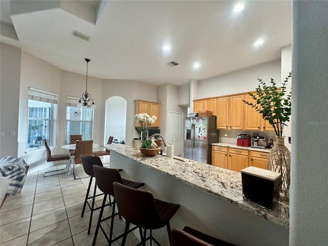 kitchen with arched walkways, a sink, tasteful backsplash, visible vents, and stainless steel refrigerator with ice dispenser
