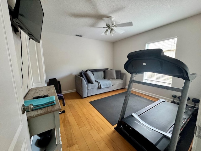 workout area with a textured ceiling, baseboards, visible vents, a ceiling fan, and hardwood / wood-style floors