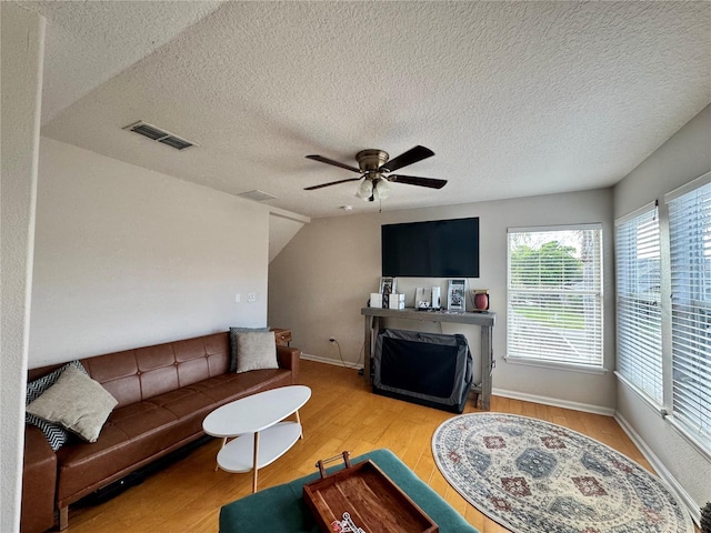 living room with wood finished floors, visible vents, a ceiling fan, baseboards, and a textured ceiling