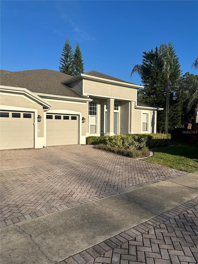 view of front of home with stucco siding, a shingled roof, decorative driveway, and a garage