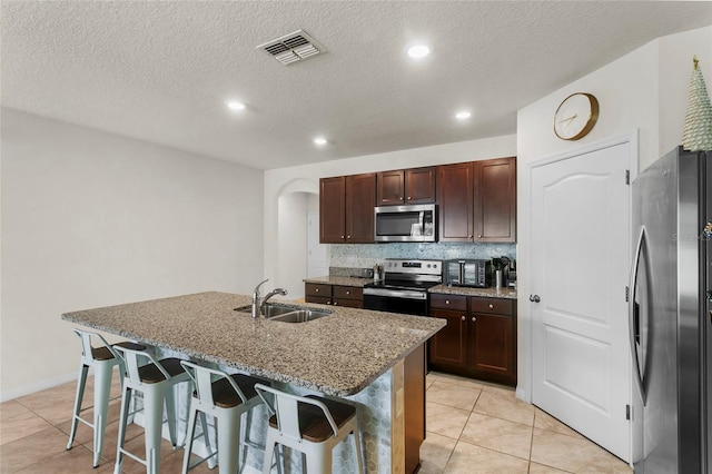 9005 Tuscan Cypress St, Kissimmee, FL 34747 - kitchen with stainless steel appliances, a breakfast bar area, arched walkways, a kitchen island with sink, and light tile patterned flooring
