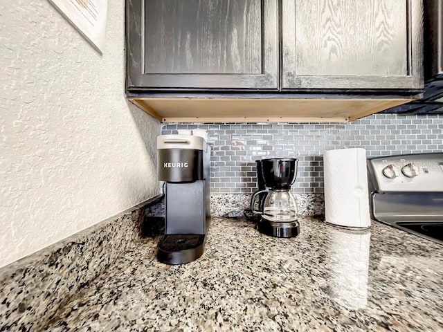 kitchen view of decorative backsplash, a textured wall, dark brown cabinets, light stone counters, and range