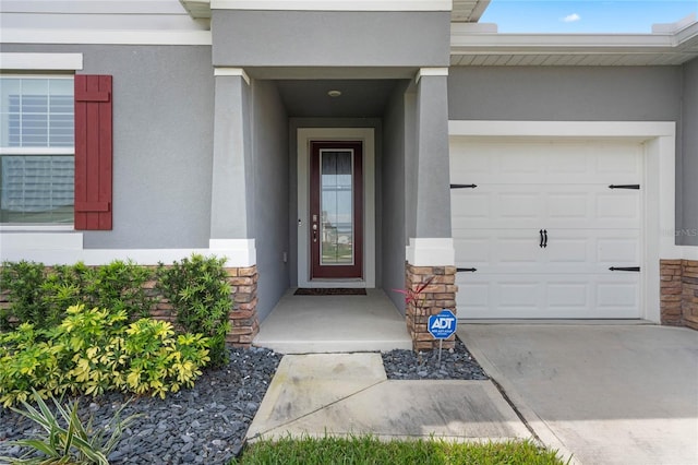 view of exterior entry with stucco siding, an attached garage, stone siding, and concrete driveway