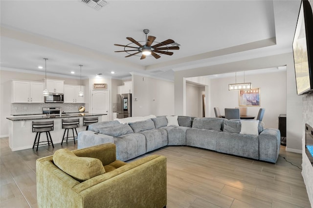 living area with ceiling fan with notable chandelier, visible vents, crown molding, and a raised ceiling