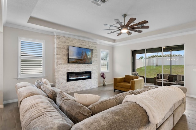 living room with a tray ceiling, visible vents, ceiling fan, and wood finished floors