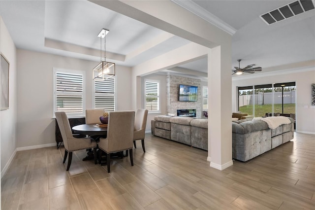 dining room featuring light wood-style flooring, visible vents, baseboards, a fireplace, and a raised ceiling