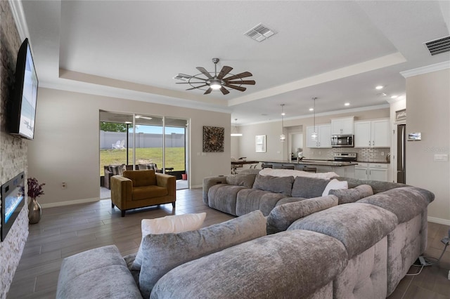 living area with a fireplace, visible vents, a ceiling fan, and a raised ceiling