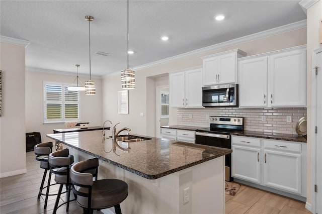 kitchen with crown molding, stainless steel appliances, an island with sink, a sink, and backsplash