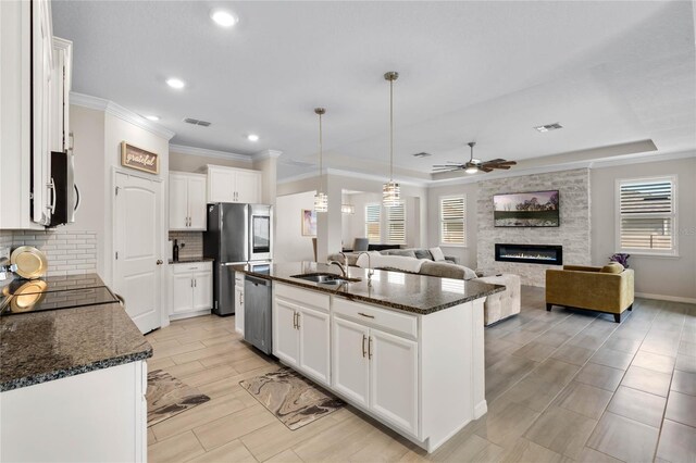 kitchen with decorative backsplash, a large fireplace, a sink, ceiling fan, and appliances with stainless steel finishes