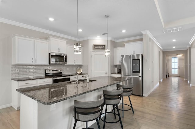 kitchen featuring a kitchen breakfast bar, a sink, visible vents, white cabinets, and appliances with stainless steel finishes