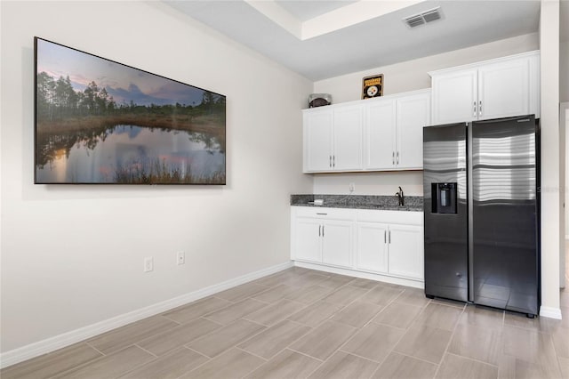 kitchen featuring stainless steel fridge, baseboards, visible vents, white cabinets, and dark stone counters
