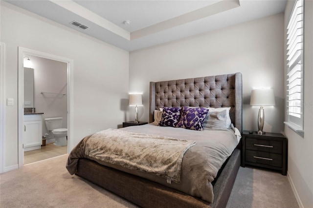 bedroom with ensuite bathroom, visible vents, baseboards, a tray ceiling, and light colored carpet
