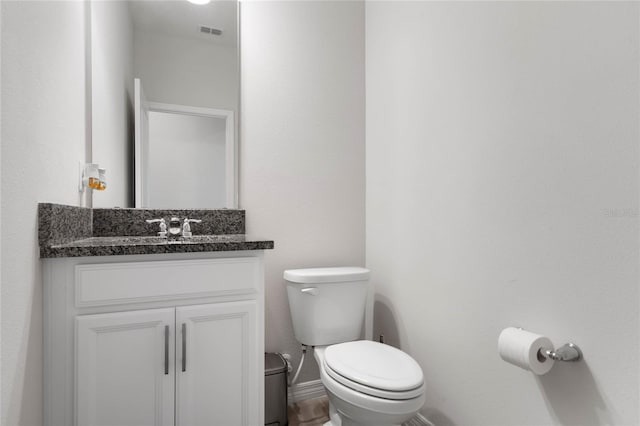 half bath featuring baseboards, visible vents, toilet, and vanity