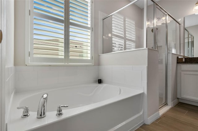 bathroom with a stall shower, wood finished floors, vanity, and a bath
