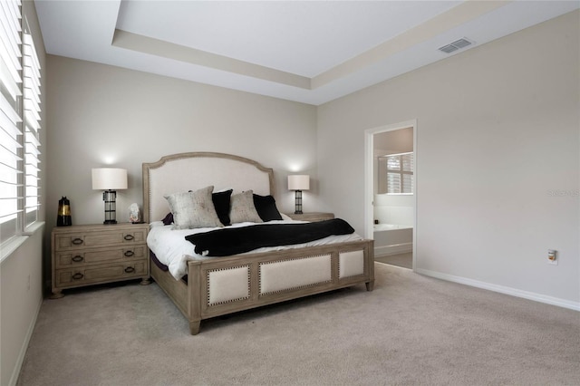 bedroom with a tray ceiling, ensuite bathroom, baseboards, light colored carpet, and visible vents