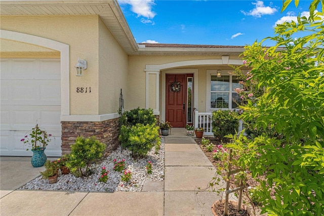 view of exterior entry with a porch, an attached garage, stucco siding, and stone siding