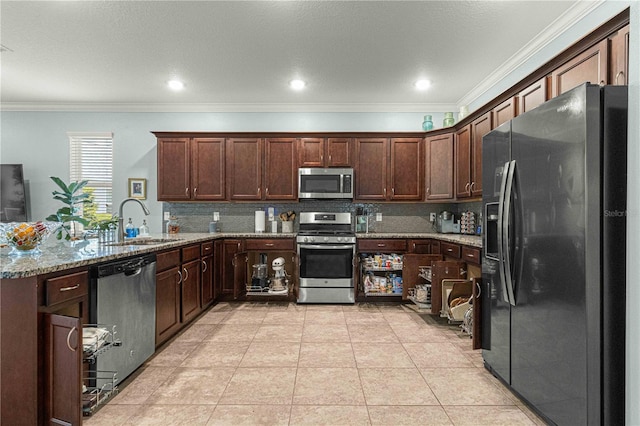 kitchen featuring light stone counters, crown molding, decorative backsplash, stainless steel appliances, and a sink
