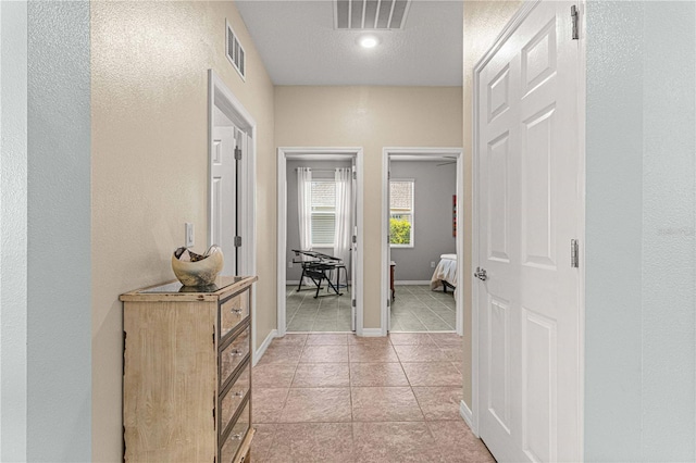 hall featuring light tile patterned floors, baseboards, and visible vents