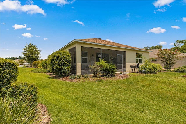 back of house with a yard, stucco siding, and a sunroom