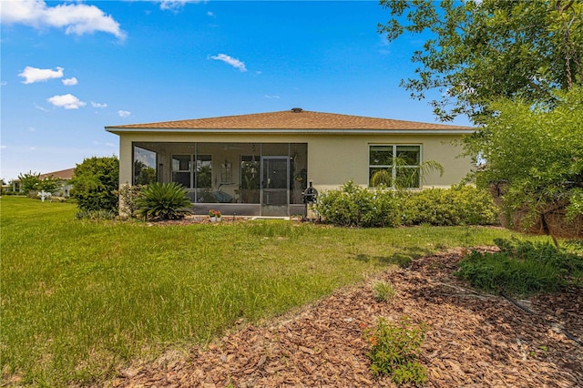 rear view of house with a yard, stucco siding, and a sunroom