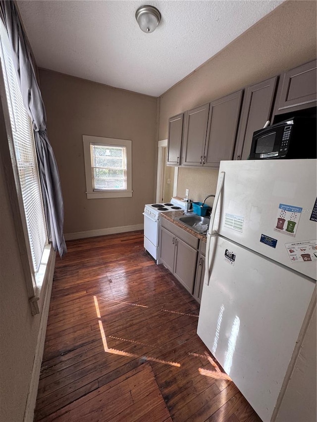 kitchen with a sink, white appliances, gray cabinets, dark wood finished floors, and baseboards