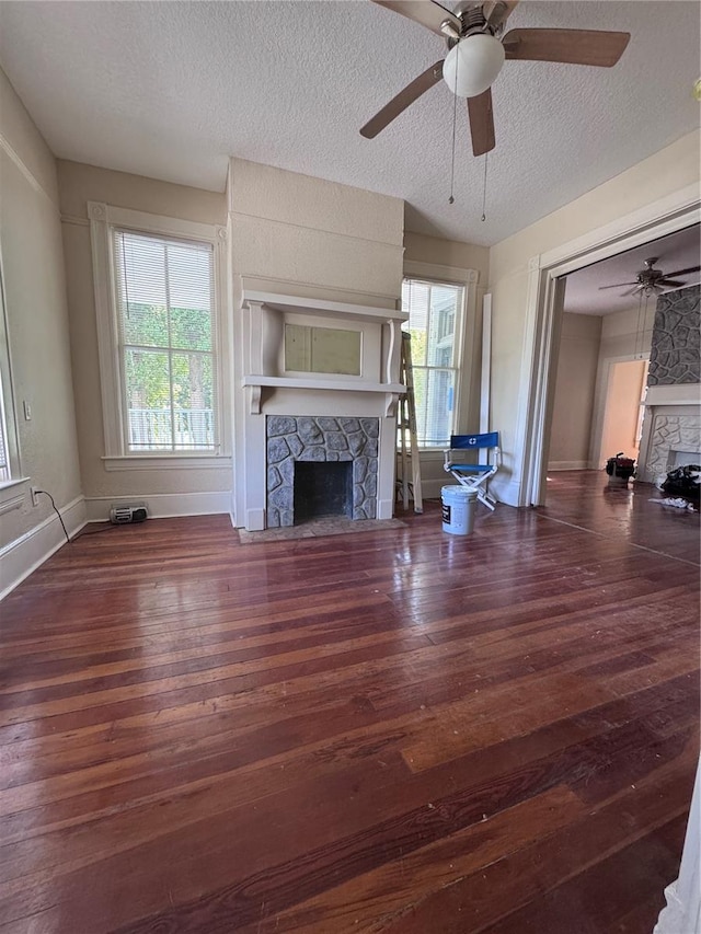unfurnished living room with a textured ceiling, baseboards, ceiling fan, a stone fireplace, and wood-type flooring