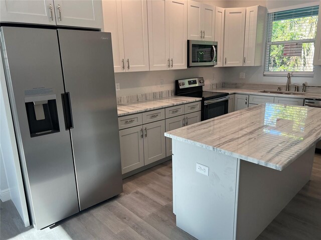 kitchen featuring a sink, light wood finished floors, stainless steel appliances, a kitchen island, and light stone counters