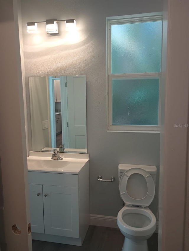 half bath with toilet, baseboards, and vanity
