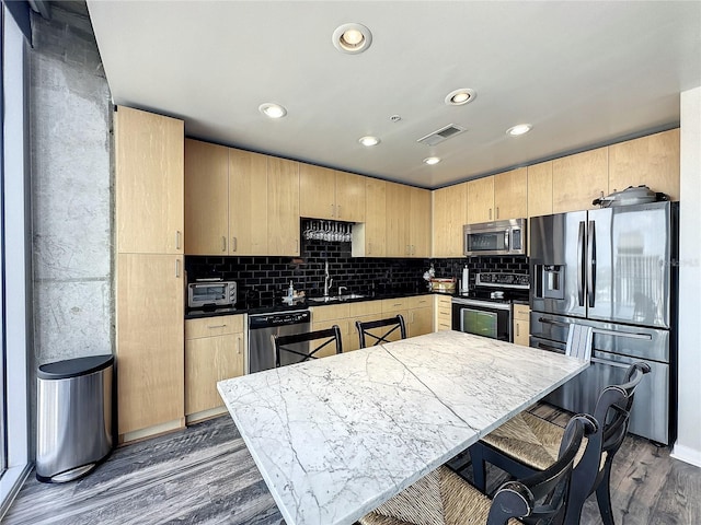 kitchen with a sink, stainless steel appliances, light brown cabinetry, and dark wood finished floors