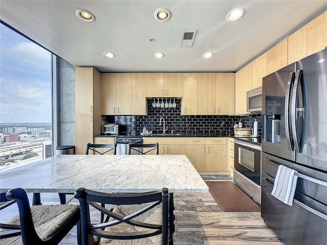 kitchen featuring dark countertops, stainless steel appliances, a sink, backsplash, and light brown cabinetry