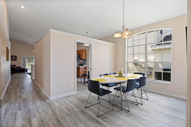 dining space featuring baseboards, vaulted ceiling, a notable chandelier, and wood finished floors