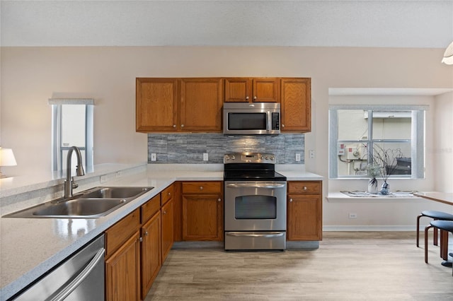 kitchen with light countertops, a sink, backsplash, appliances with stainless steel finishes, and brown cabinets