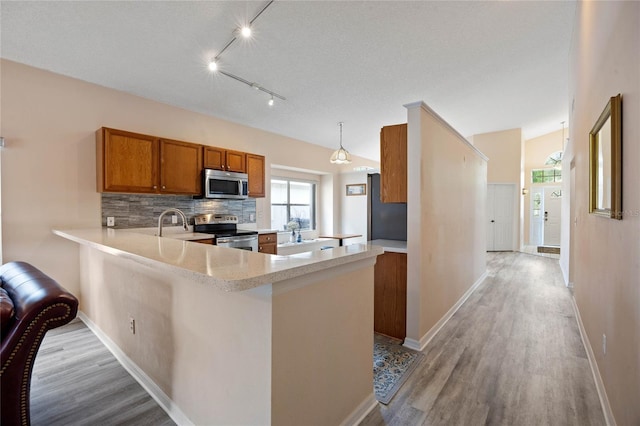 kitchen with light countertops, tasteful backsplash, a peninsula, appliances with stainless steel finishes, and brown cabinetry