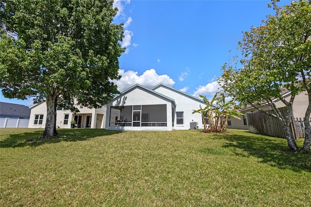 rear view of house featuring stucco siding, a sunroom, fence, and a yard