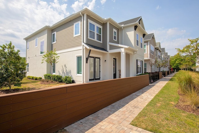 view of property exterior featuring stucco siding, fence, and a residential view