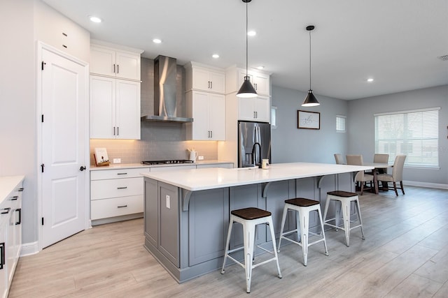 kitchen with decorative backsplash, stainless steel fridge, cooktop, an island with sink, and wall chimney range hood