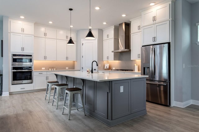 kitchen with light countertops, a sink, wall chimney exhaust hood, and appliances with stainless steel finishes
