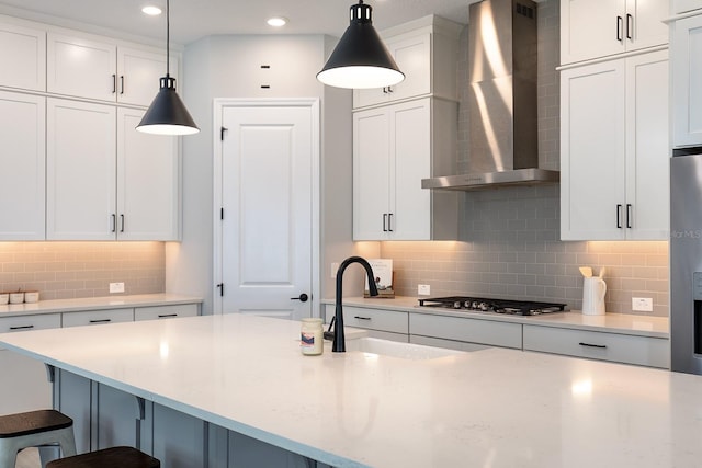 kitchen with a kitchen breakfast bar, a sink, stainless steel gas stovetop, wall chimney range hood, and white cabinets