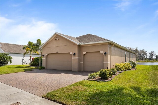 3936 Parkhouse Dr, Orlando, FL 32824 - view of home's exterior featuring a water view, decorative driveway, a garage, stucco siding, and a yard