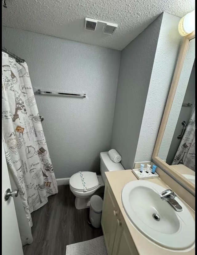 bathroom with a textured ceiling, visible vents, wood finished floors, toilet, and a textured wall