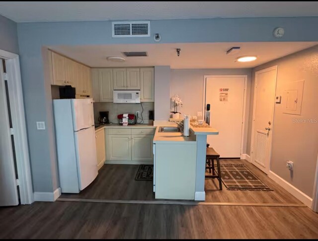kitchen featuring a sink, a peninsula, white appliances, visible vents, and dark wood-type flooring