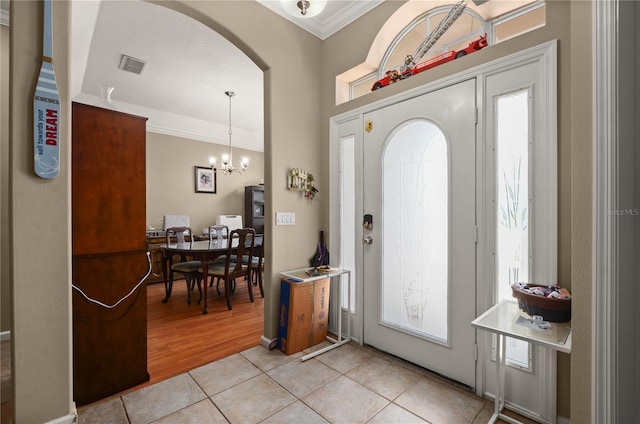 625 Waterland Ct, Orlando, FL 32828 - entryway featuring light tile patterned flooring, visible vents, a chandelier, crown molding, and arched walkways