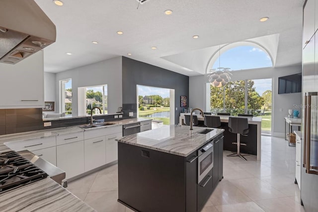 9000 Shawn Park Pl, Orlando, FL 32819 - kitchen with light stone counters, a sink, modern cabinets, wall chimney range hood, and a kitchen island with sink