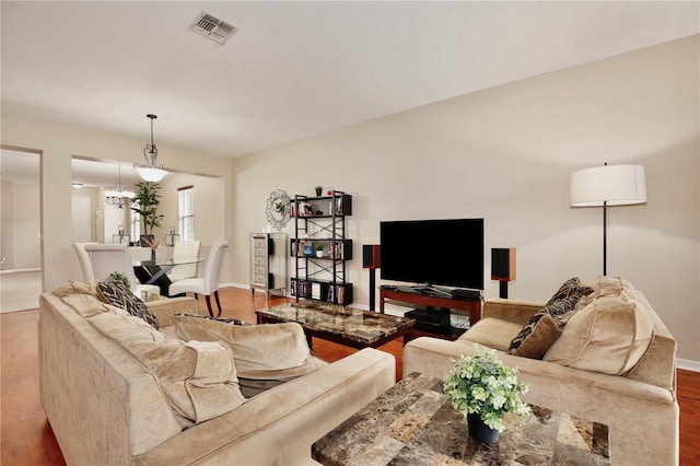 living area with a notable chandelier, visible vents, wood finished floors, and baseboards