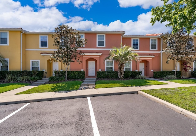 multi unit property featuring a front lawn, uncovered parking, a tile roof, and stucco siding