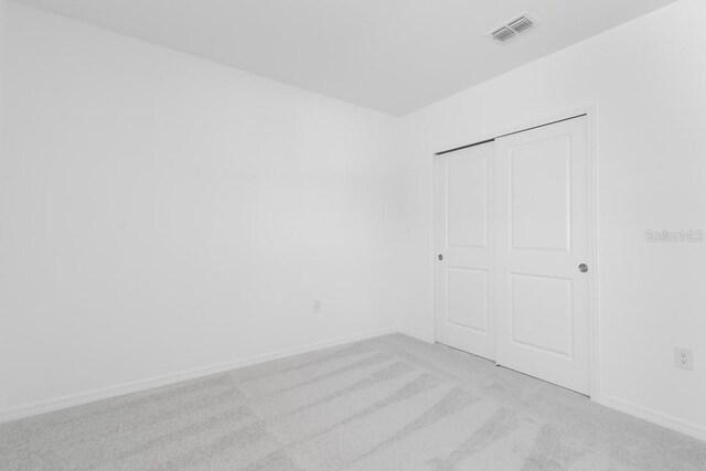 unfurnished bedroom featuring a closet, visible vents, baseboards, and light carpet