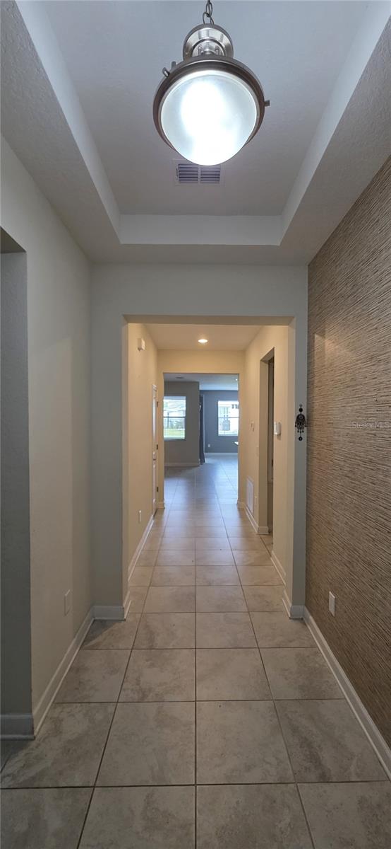 3043 Beaver Creek Dr, Kissimmee, FL 34746 - hall with light tile patterned flooring, visible vents, baseboards, and a tray ceiling